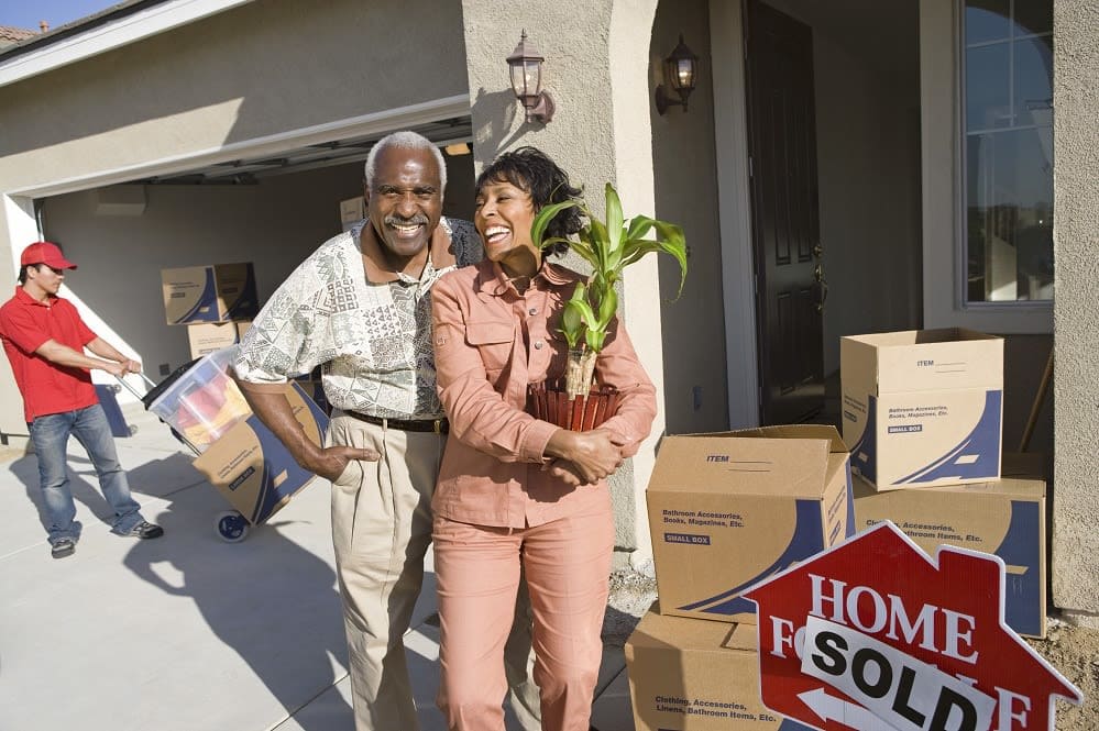 Cheerful African American couple with belongings moving into a new house title=